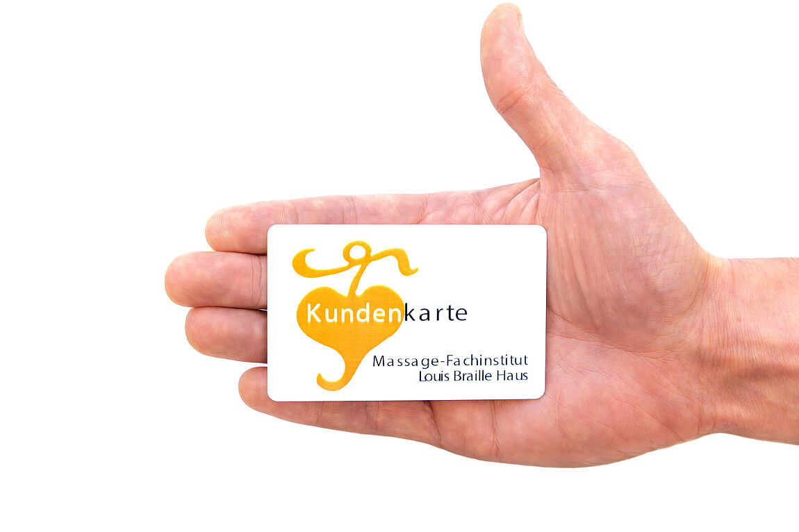 © BSVWNB/ Michael Schrenk Hand hält eine weiße Kundenkarte mit orangefarbenem Logo und der Aufschrift 'Massage-Fachinstitut Louis Braille Haus'